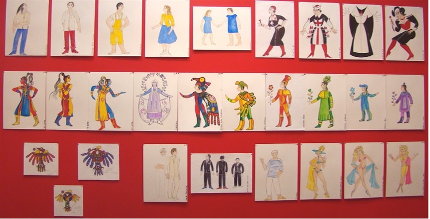 This image shows a vibrant wall display of costume design sketches arranged neatly against a bright red background. The sketches showcase diverse costume concepts, ranging from everyday attire to elaborate and theatrical outfits with bold colors and detailed designs, reflecting creative and expressive character interpretations.